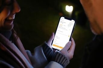 **Alt-Text:** Person steuert eine Steinel Außenleuchte über eine Smartphone-App im Garten bei Nacht.
