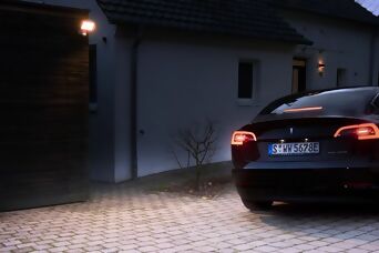 **Alt-Text:** Ein beleuchteter Hauseingang mit Steinel Außenleuchte und parkendem Auto in der Einfahrt bei Dämmerung.