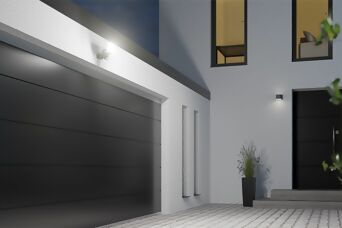 Das Bild zeigt eine moderne Hausfassade mit einer beleuchteten Garage und Hauseingang, ausgestattet mit der Steinel XLED Protect S. Der leistungsstarke LED-Strahler über der Garage bietet eine helle und flächige Ausleuchtung, die durch den integrierten Bew