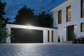 Das Bild zeigt eine modern gestaltete Einfahrt mit einer beleuchteten Garage und einem Hauseingang, ausgestattet mit der **Steinel XLED Protect S**. Der leistungsstarke LED-Strahler sorgt für eine großflächige und helle Beleuchtung der Zufahrt, wodurch Sic