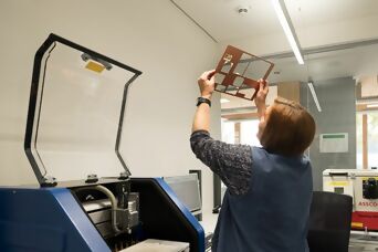 Mitarbeiterin in der Qualitätskontrolle prüft eine Leiterplatte unter Licht in einem modernen Labor.