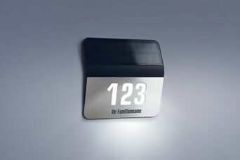 Beleuchtete, personalisierte Solar-Hausnummer „123“ mit Familienname, montiert an einer Hauswand.