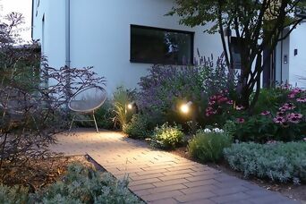 Stimmungsvolle Gartenbeleuchtung mit Steinel Spots entlang eines gepflasterten Weges und blühenden Pflanzen.